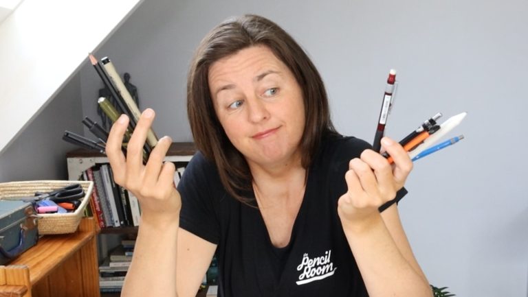 Photo of art tutor holding up drawing tools including pencils and pens