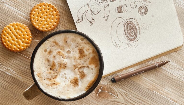 photo showing a cup of coffee and biscuits next to a sketchbook